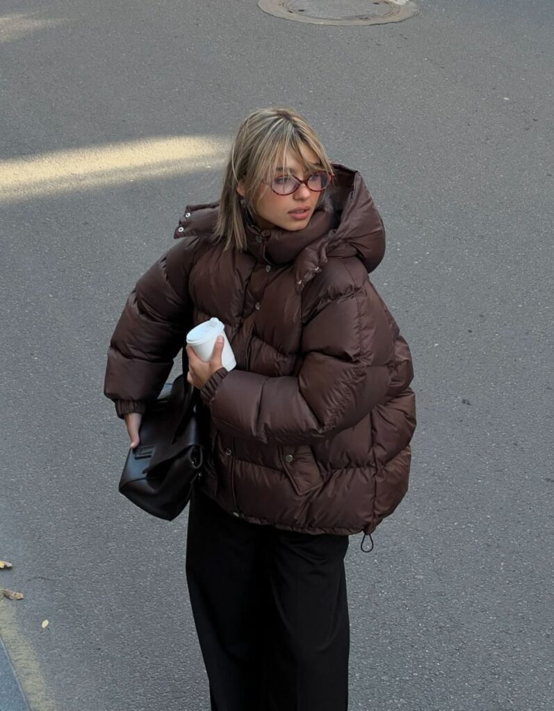 Lady putting in a brown puffer jacket in the winter 